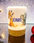 Erleuchtetes LED-Nachtlicht mit Holzsockel und Giraffen- und Elefant-Motiv, mit Namen personalisiert. Vor weihnachtlichem Hintergrund stehend.