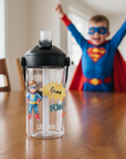 trinkflasche mit superhelden motiv mit strahlendem jungen als superheld verkleidet im hintergrund