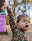 Mädchen hält pinke Klean Kanteen Kinder Trinkflasche mit Einhorn-Motiv und türkiser Verschlusskappe, mit Namen personalisierbar.