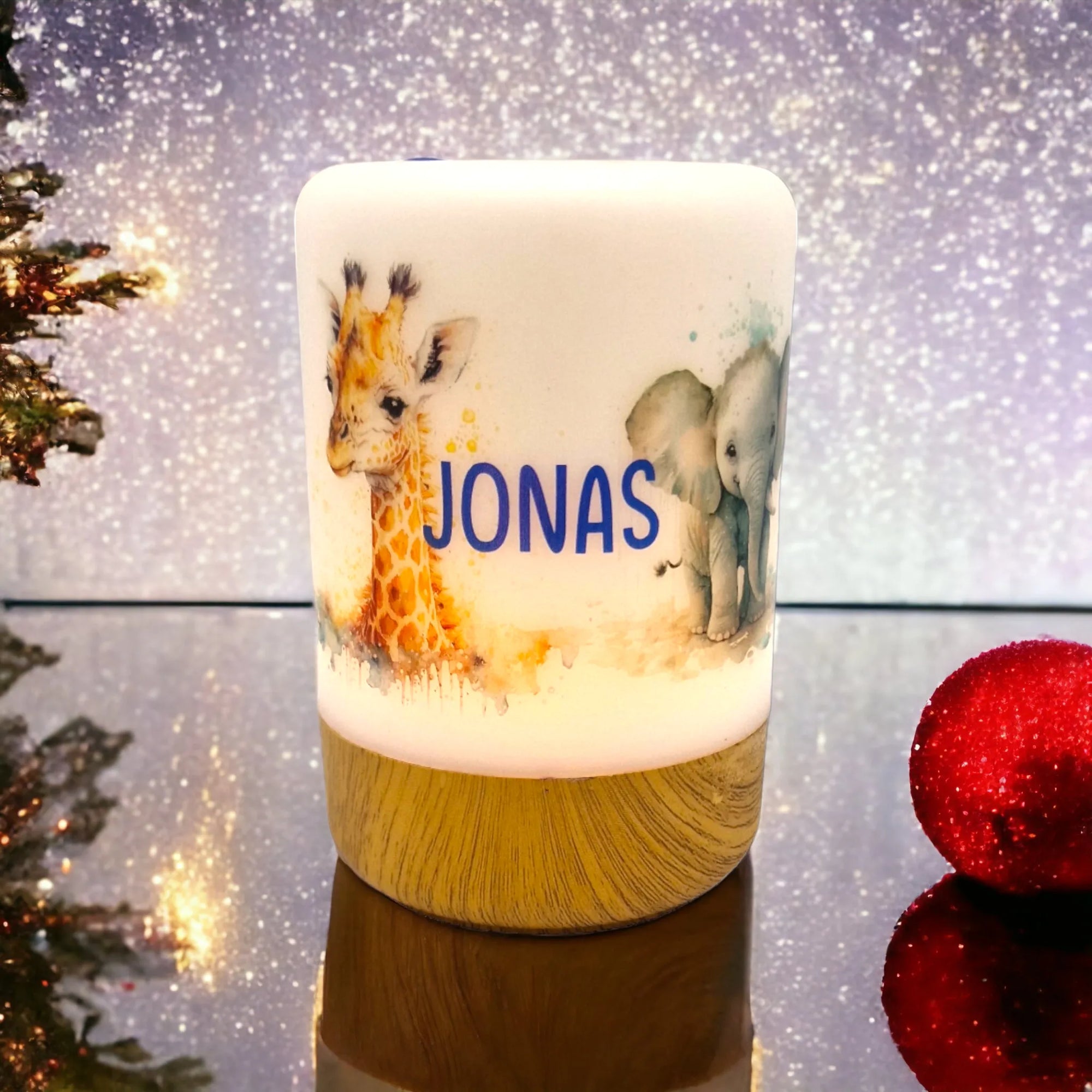 Erleuchtetes LED-Nachtlicht mit Holzsockel und Giraffen- und Elefant-Motiv, mit Namen personalisiert. Vor weihnachtlichem Hintergrund stehend.