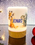 Erleuchtetes LED-Nachtlicht mit Holzsockel und Giraffen- und Elefant-Motiv, mit Namen personalisiert. Vor weihnachtlichem Hintergrund stehend.