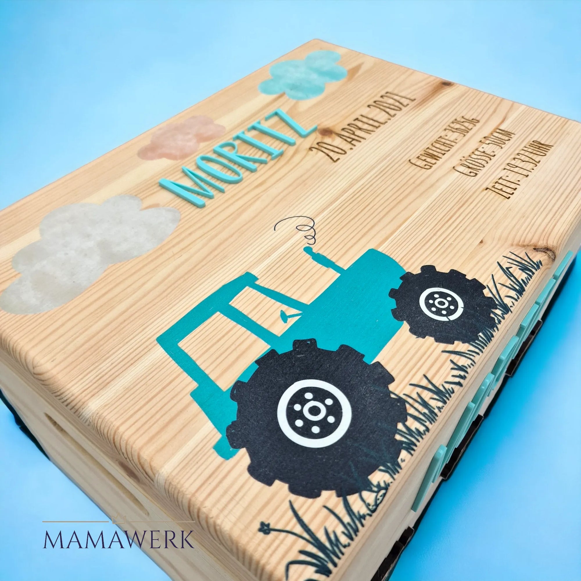 Design von holziger Erinnerkungskiste. Deckel mit blauem Traktor-Motiv sowie Wolken dekoriert und mit blauem Namen und Geburtsdaten personalisiert. Vorderseite mit drei Baustellenfahrzeugen dekoriert und mit blauem Namen personalisiert.