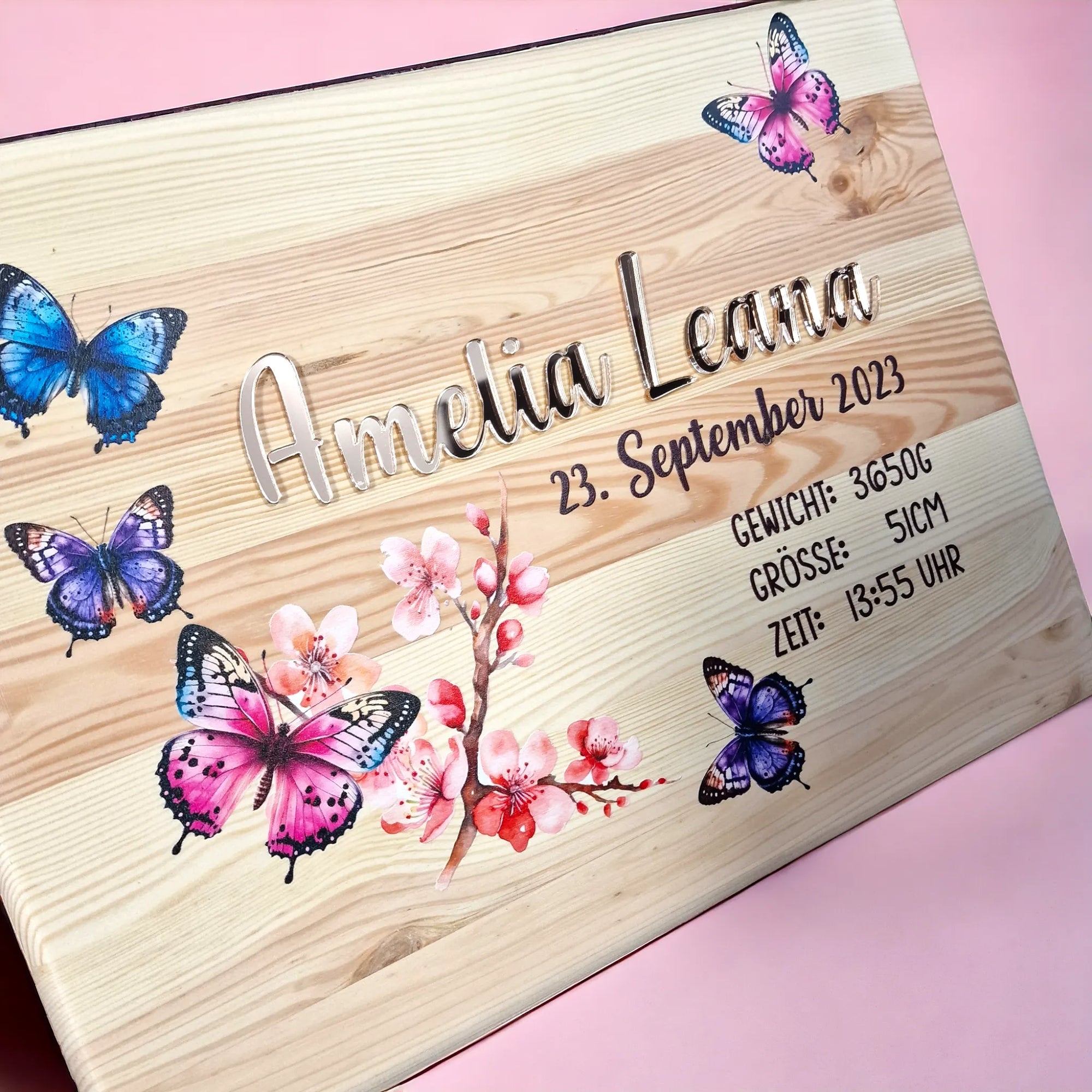 Deckel von holziger Erinnerungskiste mit Schmetterlingen und Blüte, personalisiert mit glasigem Namen und Geburtsdaten.