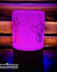 Violett erleuchtetes LED-Nachtlicht mit Holzsockel und Giraffen- und Elefant-Motiv, mit Namen personalisiert. Vor holzigem Hintergrund stehend.