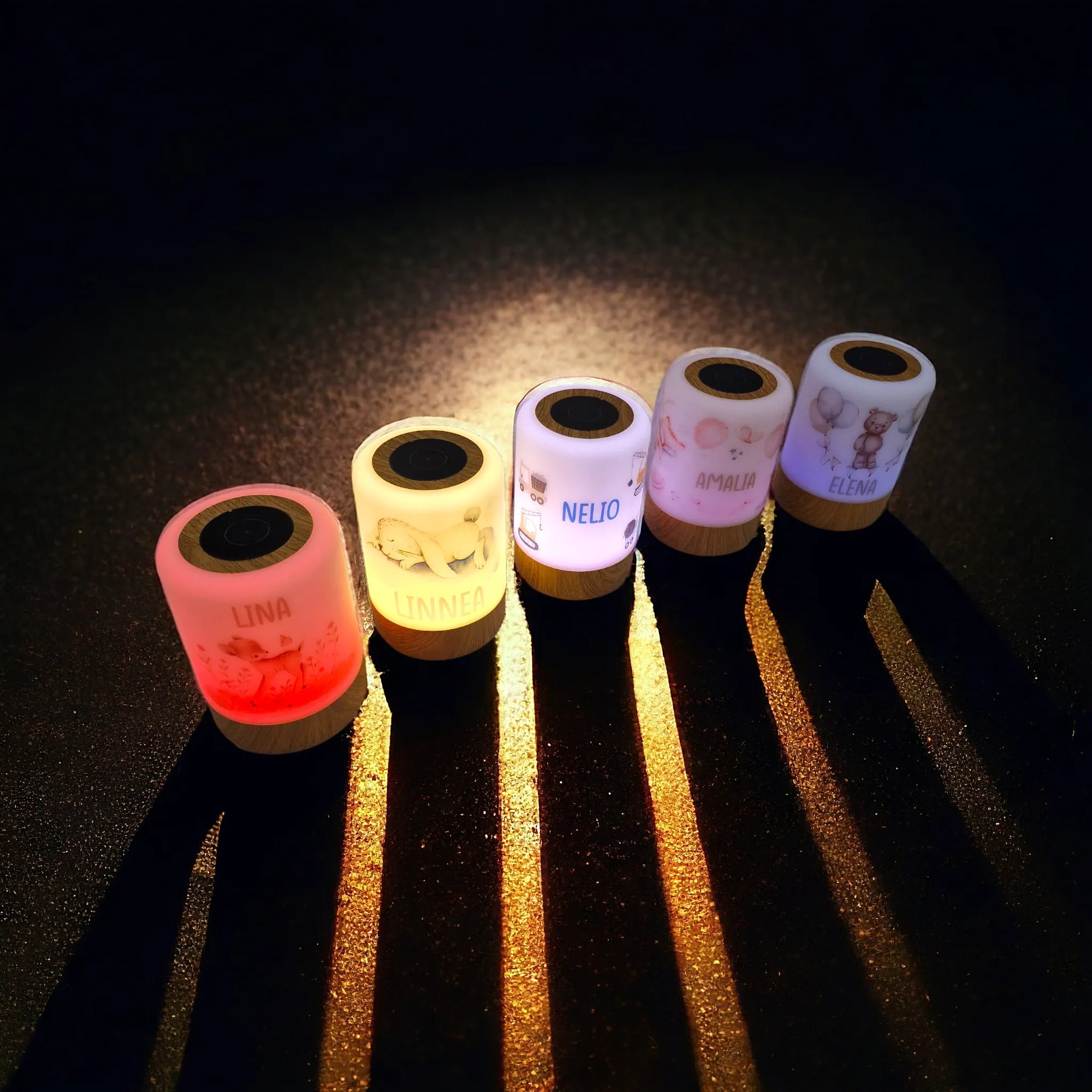 Fünf personalisierbare LED-Nachtlichter mit Boho-Tier-Motiv, in verschiedenen Farben erleuchtet, am Boden in dunklem Raum stehend.