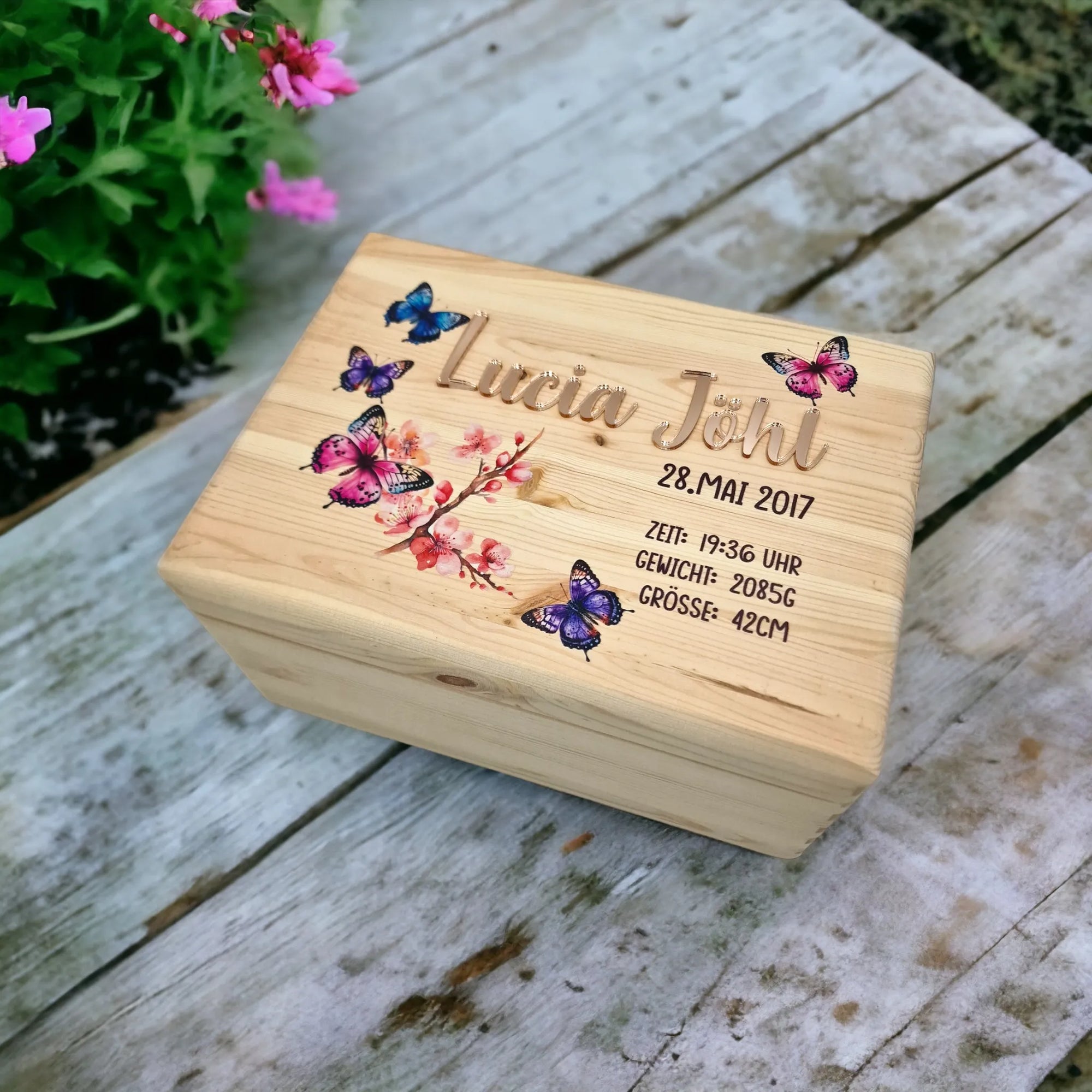 Eine Erinnerungskiste mit Schmetterlingen und Blüte auf Deckel sowie personalisiert mit goldenem Namen und Geburtsdaten.