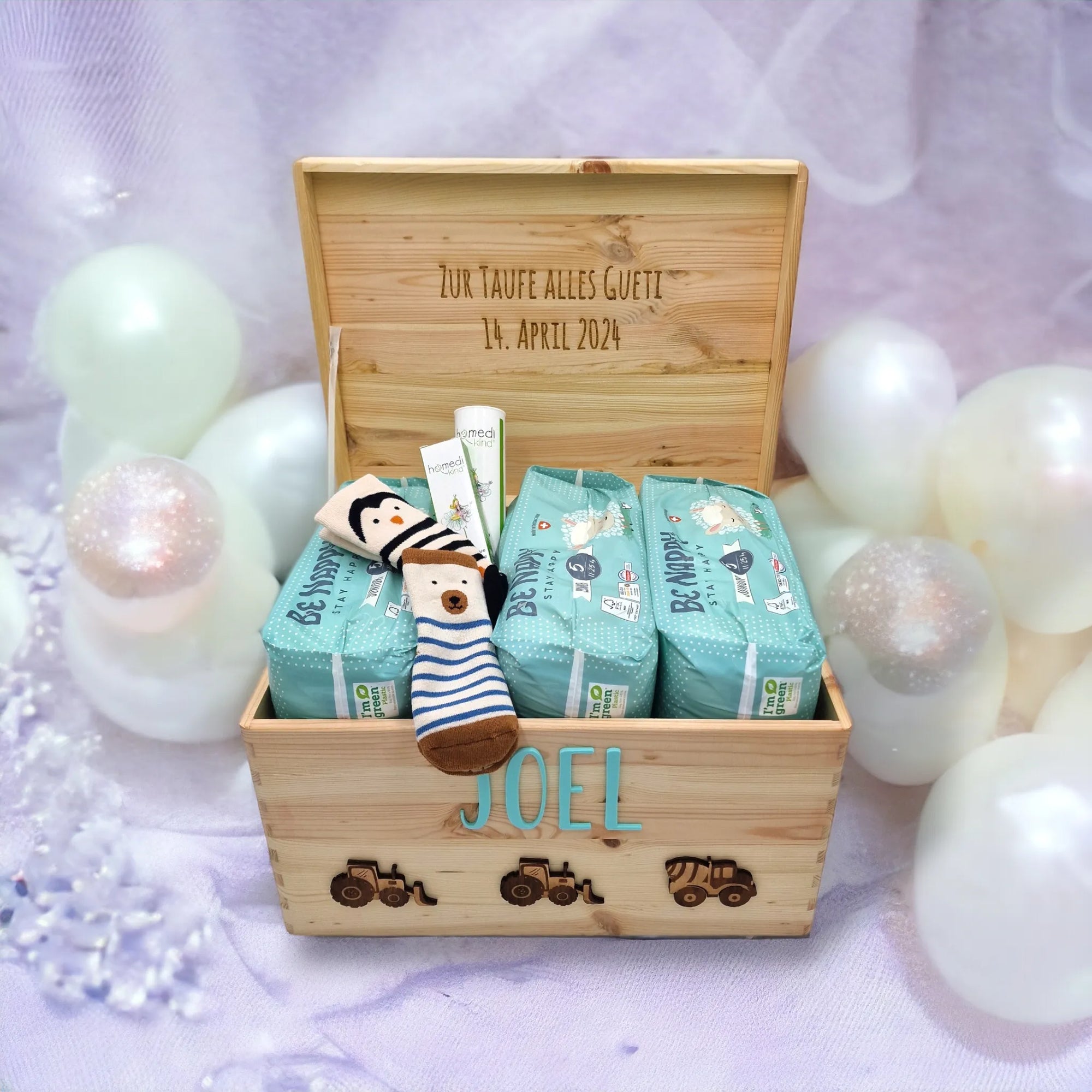 Ein Taufgeschenk für Jungen. Eine Baustellen Fahrzeug Erinnerungskiste, personalisiert mit Namen und einer persöönlichen WIdmung auf der Innenseite des Deckels. In der Kiste sind drei Packungen Windeln, Socken und Pflegecreme.