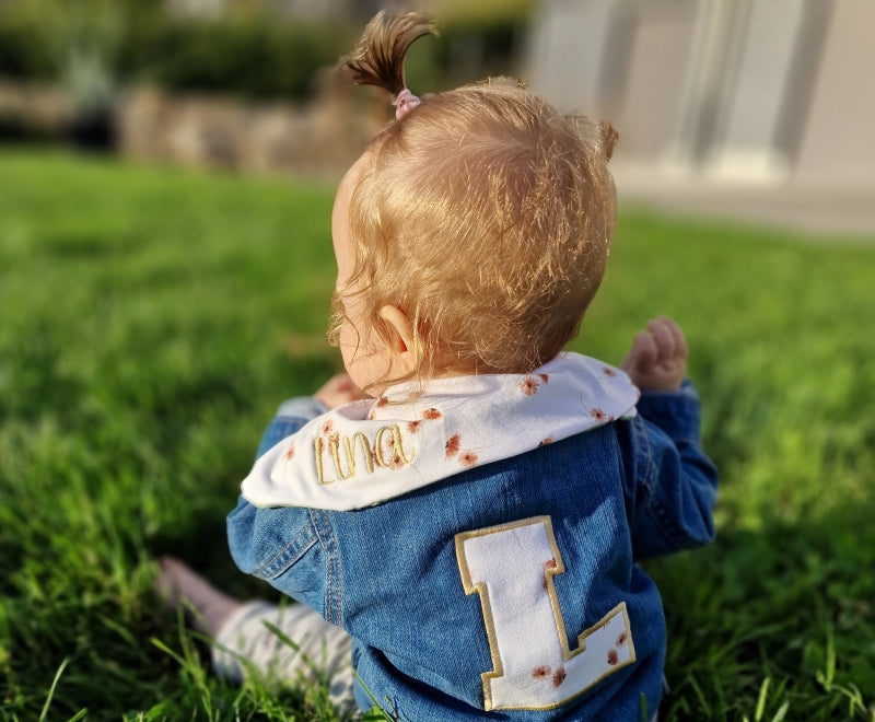 baby-in-wiese-jeansjacke-blau-mit-buchstaben-und-dreieckstuch-mit-lina