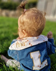 baby-in-wiese-jeansjacke-blau-mit-buchstaben-und-dreieckstuch-mit-lina