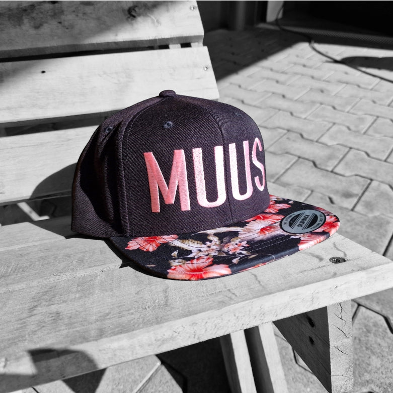flexfit caps snapback und farbigem Schild mit muus motiv gestickt in rosa auf holzstuhl