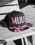 flexfit caps snapback und farbigem Schild mit muus motiv gestickt in rosa auf holzstuhl