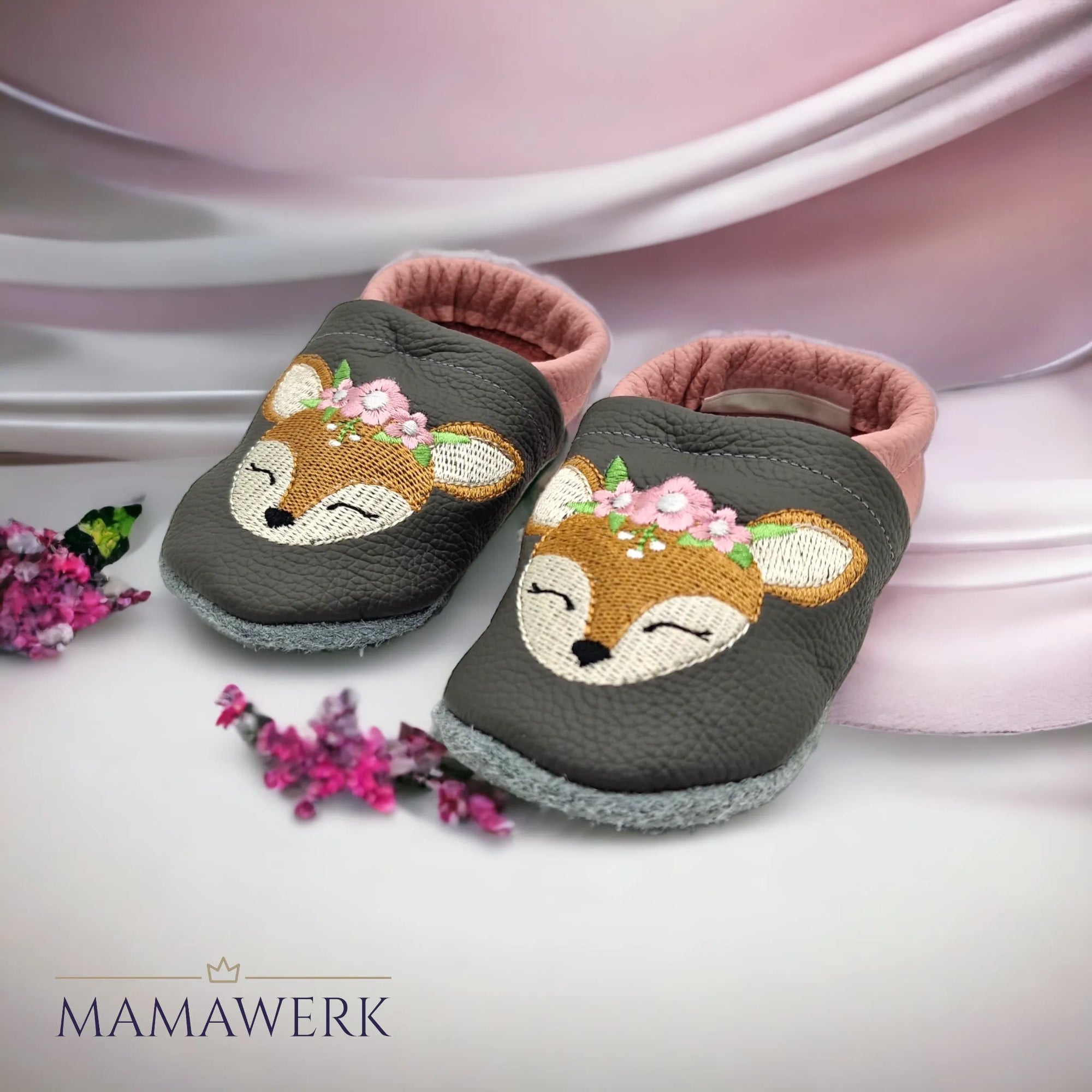 Ein Paar Rosa Lederfinken für Kinder mit grauem Oberleder auf weiss-rosa Tuch stehend. Krabbelfinken sind mit Boho-Reh Motiv bestickt. Die Sohle ist aus grauem Leder und rutschfest.
