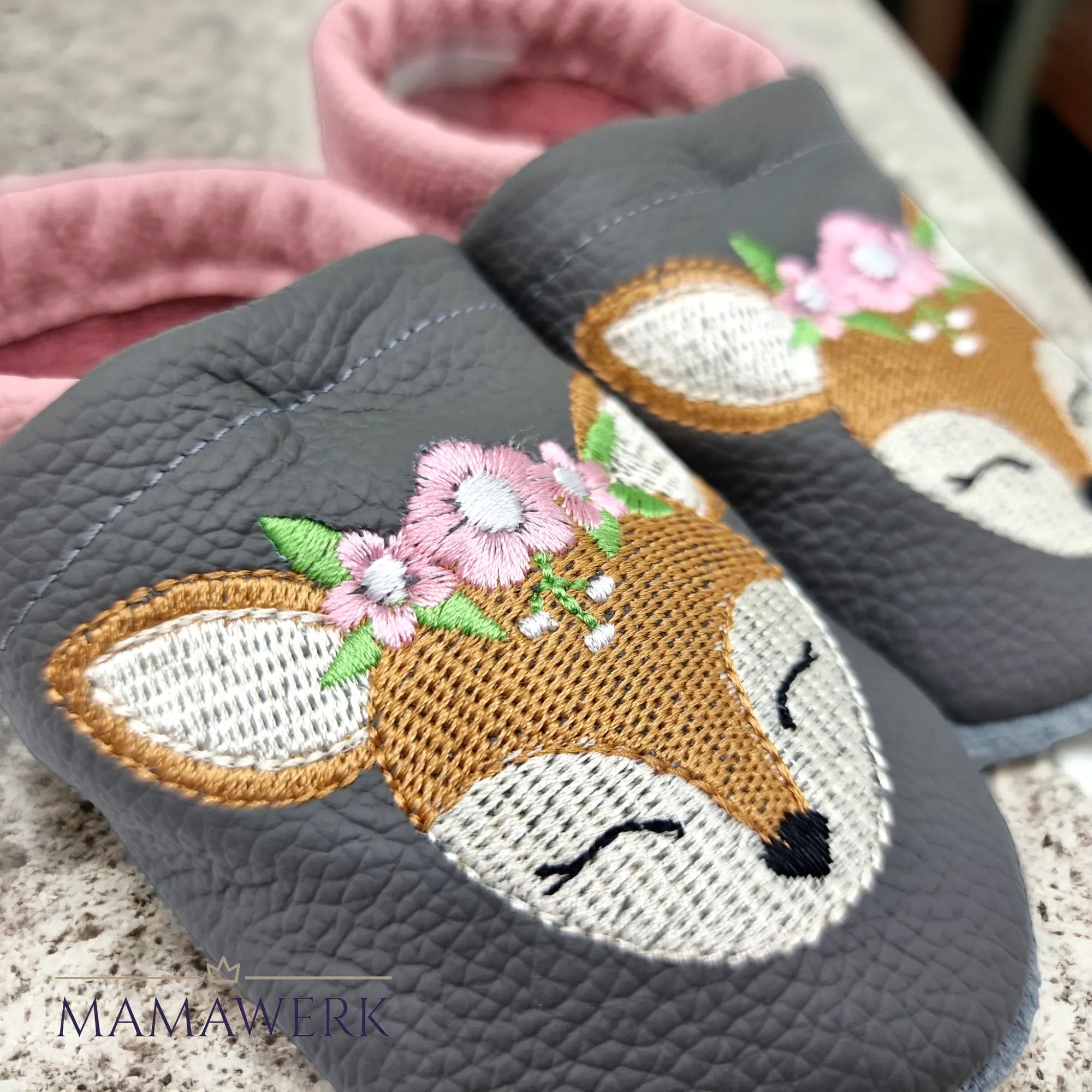 Nahaufnahme von rosa Lederfinken für Kinder mit grauem Oberleder auf Spitzdecke stehend. Krabbelfinken sind mit Boho-Reh Motiv bestickt. Die Sohle ist aus grauem Leder und rutschfest.