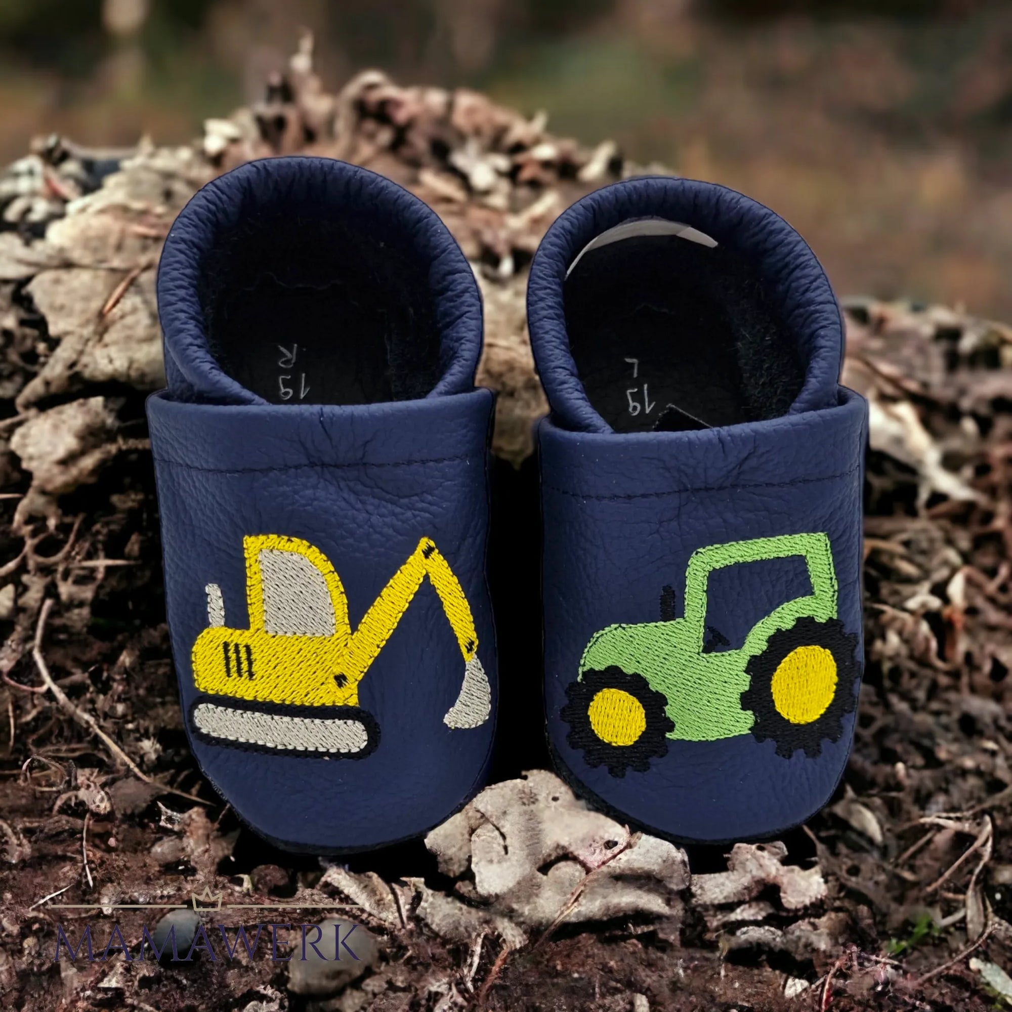 Ein Paar dunkelblaue Lederfinken für Kinder auf Erdboden platziert. Krabbelfinken sind mit Bagger und Traktor auf Oberleder bestickt. Die Sohle ist aus schwarzem Leder und rutschfest.