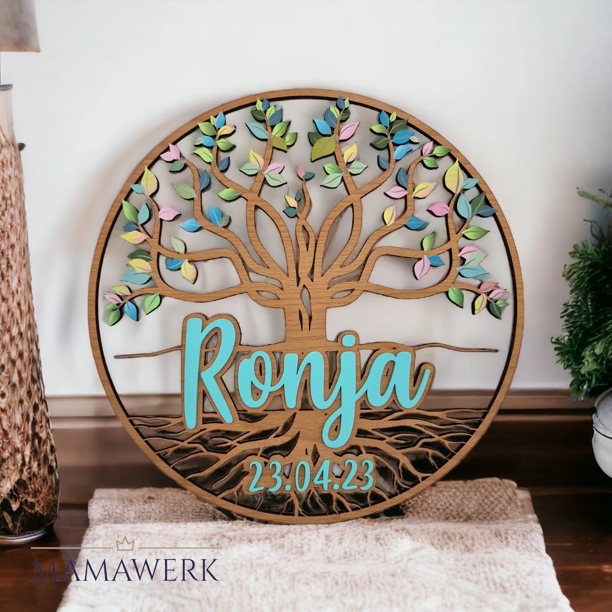 Rundes Namensschild von Mamawerk aus Holz, mit blauem Namen und Geburtsdatum aus Acrylglas sowie Lebensbaum mit farbigen Blättern bedruckt.