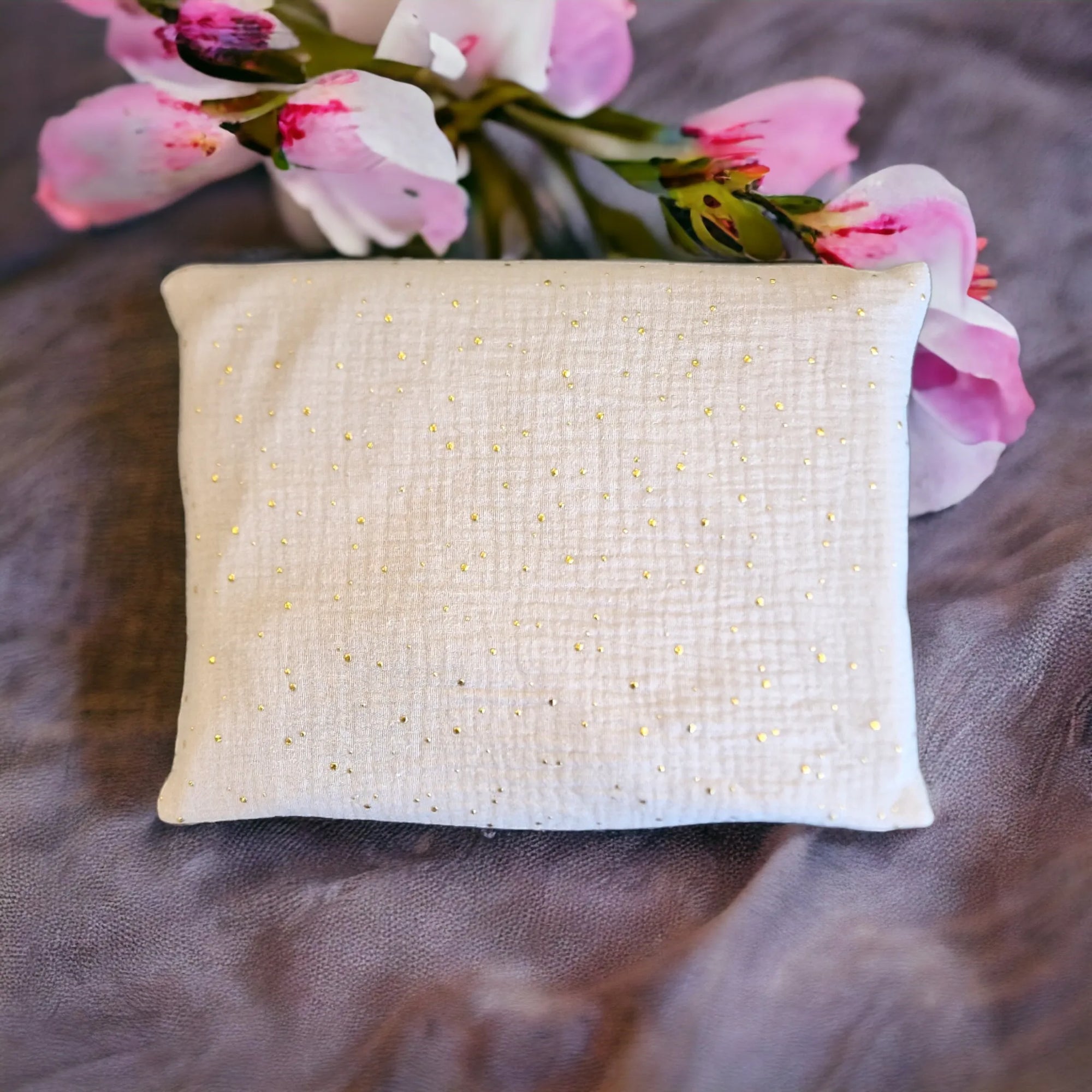 Kirschkernkissen als Wärmekissen, mit beigem Baumwollstoff und goldenen Tüpfchen, mit Blumen im Hintergrund.